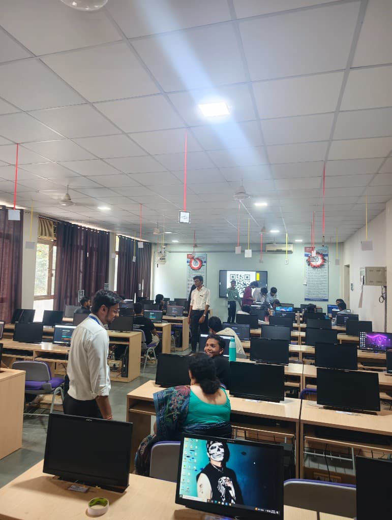 The CyberForge lab in session, with a check-in QR on the screen and strings hanging from the ceiling.