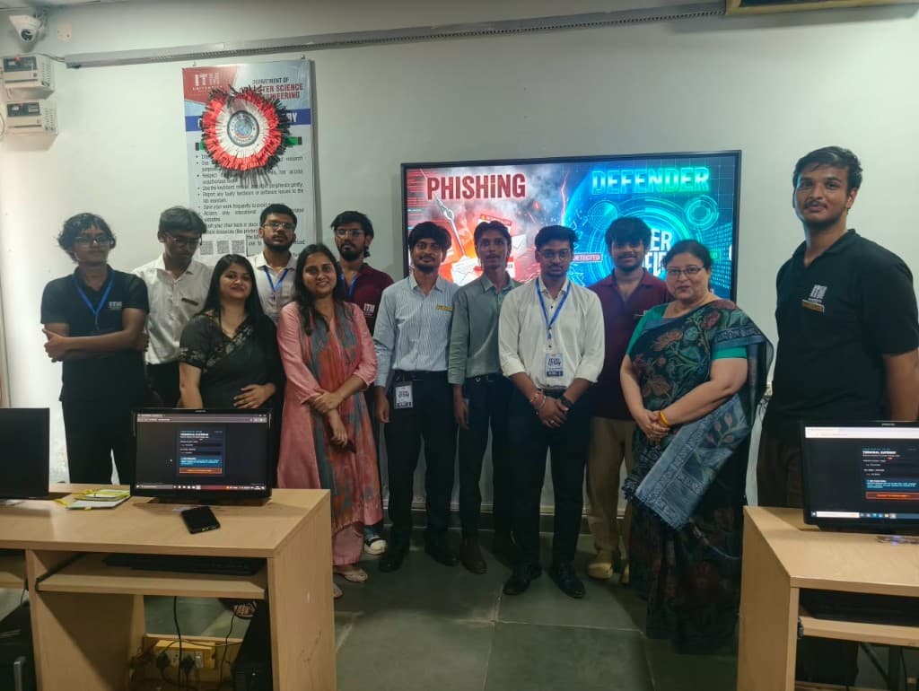 A larger CyberForge group lined up in the lab beneath the Phishing Defender display.